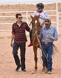 One coach lead horse athlete is riding while other coach assists beside horse.Picture