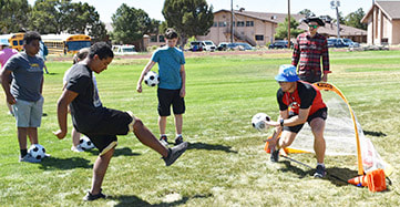 Picture Athelete kicks adaptive soccer ball with bells toward goalie/coach.