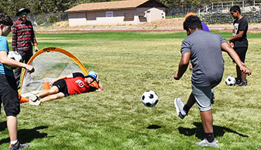 Athlete kicks adaptive soccer ball toward goalie/coach.Picture